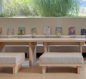A long wooden bench with cushioned seating and a wall decorated with various colorful posters.