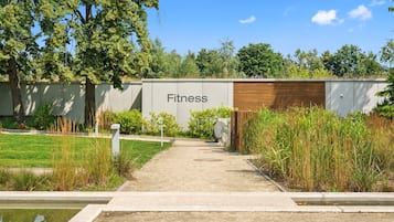 A pathway leading to a building labeled 'Fitness' with a concrete floor, surrounded by greenery and trees.