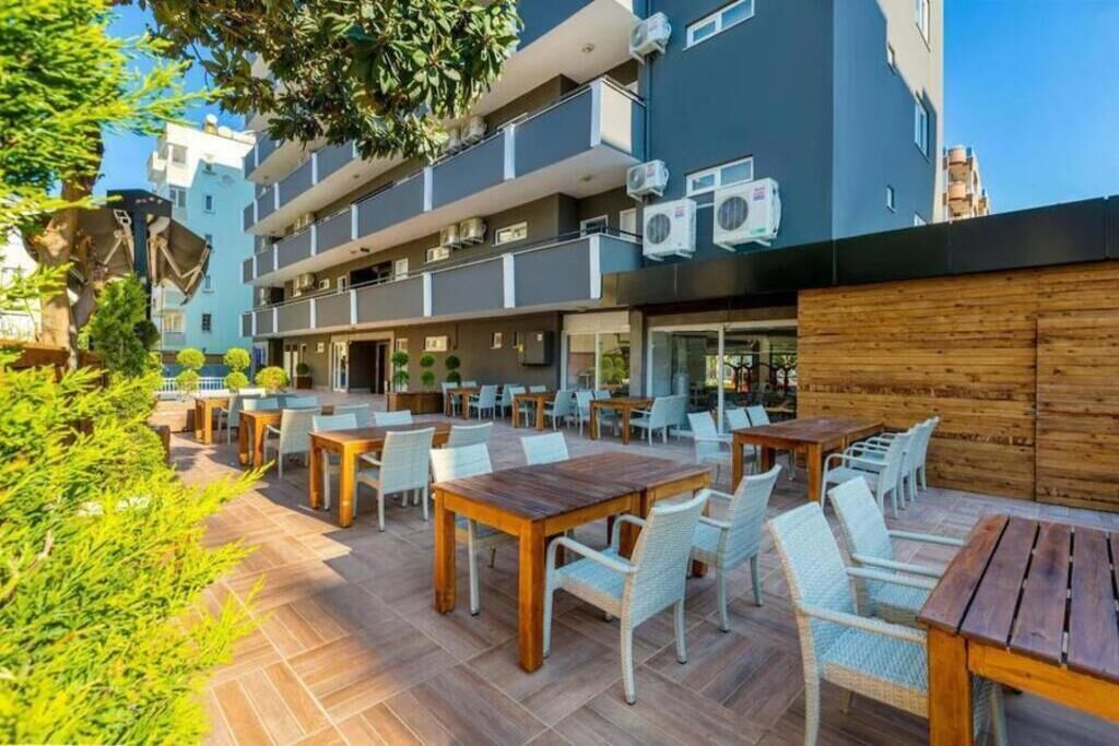 Un patio al aire libre con varias mesas y sillas, rodeado por un edificio con balcones y unidades de aire acondicionado.