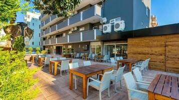 Un patio al aire libre con varias mesas y sillas, rodeado por un edificio con balcones y unidades de aire acondicionado.