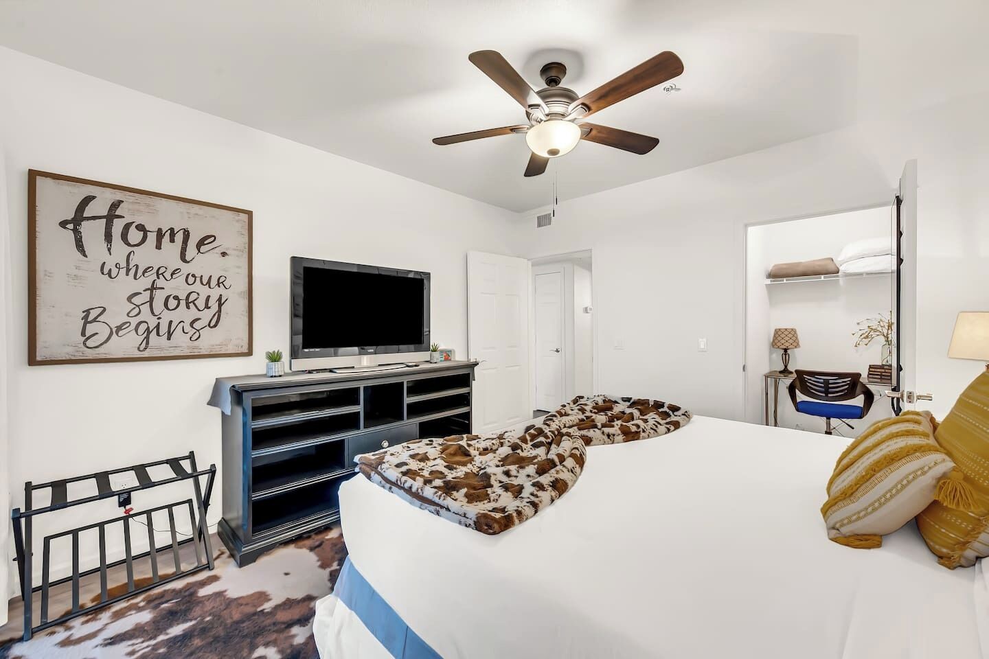 A bedroom with a large bed, a ceiling fan, a television, and a motivational wall sign.