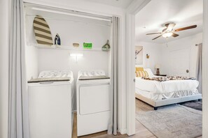 A hotel room with a bed, a ceiling fan, and a laundry area with two washing machines.