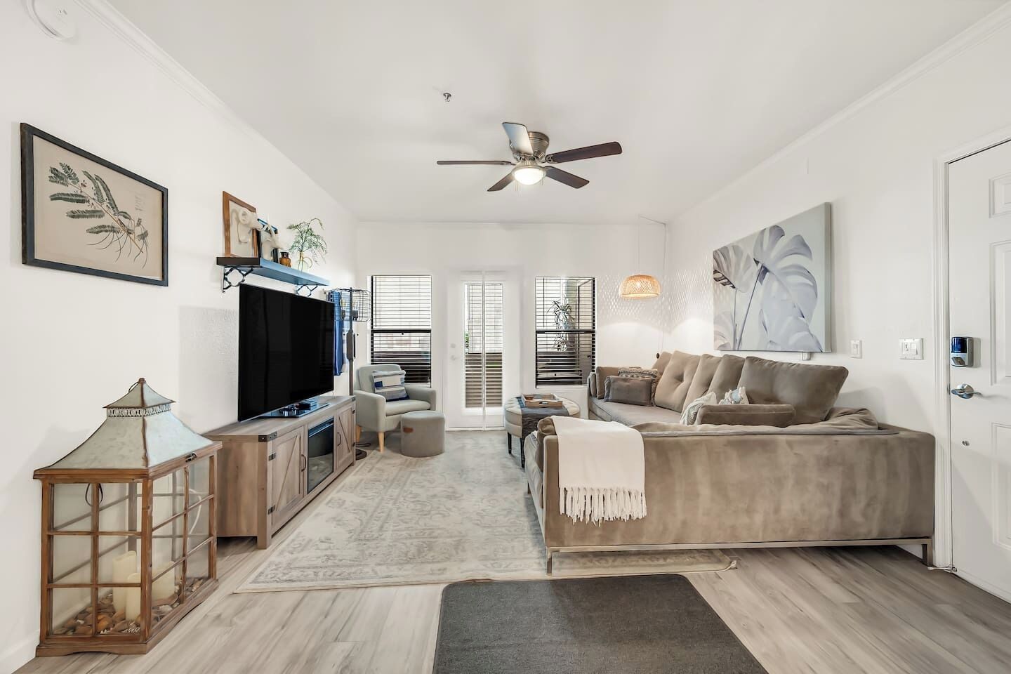 A modern living room with a flat-screen TV, a ceiling fan, and a large window.