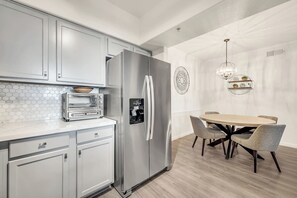 A modern kitchen with a built-in oven, a stainless steel refrigerator, and a dining area with a round table and chairs.