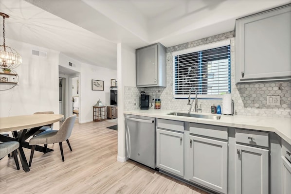 A modern kitchen with a central island, white cabinetry, and a window with blinds.