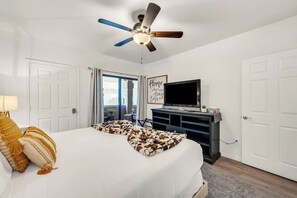 Una camera d'albergo con un letto, una ventola a soffitto, una televisione e una porta scorrevole in vetro che dà all'esterno.
