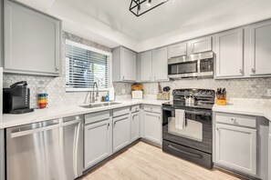 A modern kitchen with stainless steel appliances, white cabinetry, and a window with blinds.