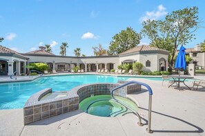 A swimming pool with a hot tub, lounge chairs, and a covered patio area.