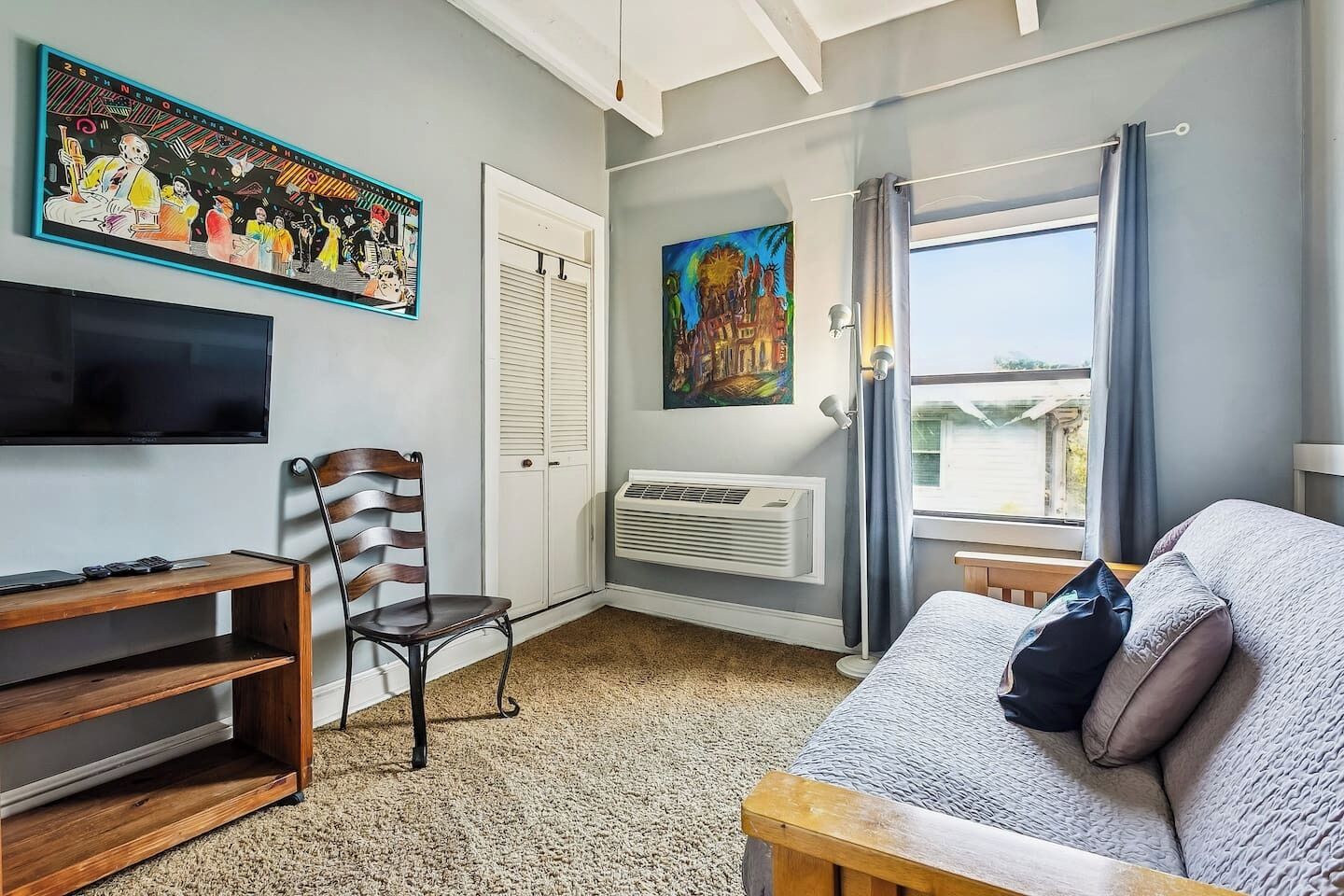 A room with a bed, a chair, a TV, a painting, and a window with curtains.
