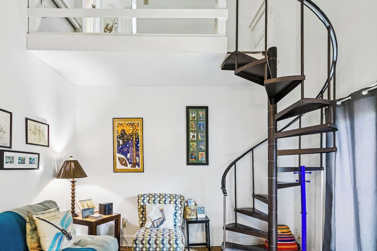 Una sala de estar con una escalera en espiral, un sofá, un sillón estampado y decoración en la pared.
