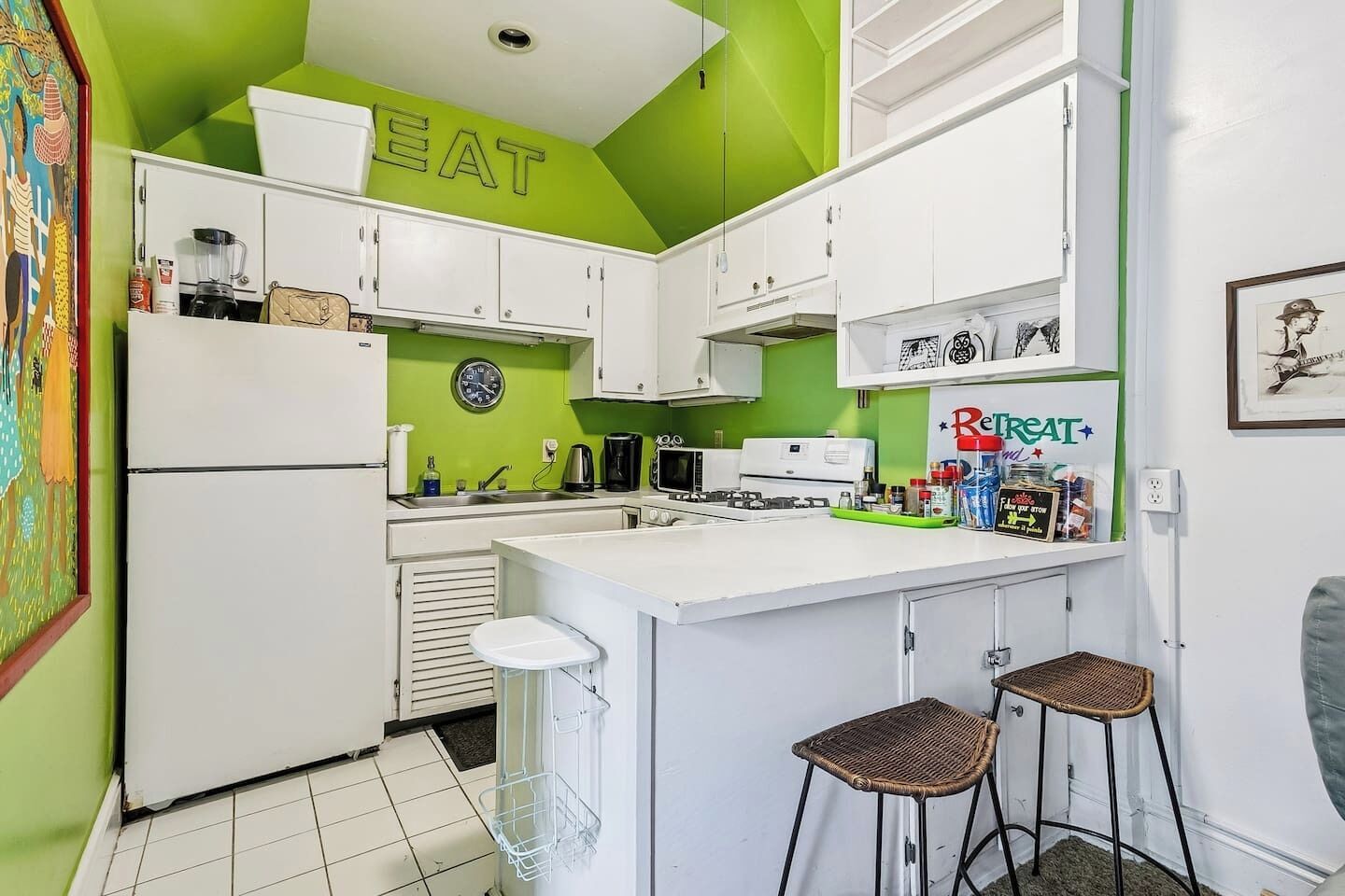 A kitchen with white cabinets, a green accent wall, a clock, and a Reptat brand refrigerator.