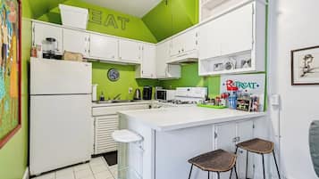 A kitchen with white cabinets, a green accent wall, a clock, and a Reptat brand refrigerator.