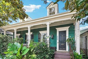 Una casa verde con un portico, una piccola torretta e il numero 3309 sul lato.