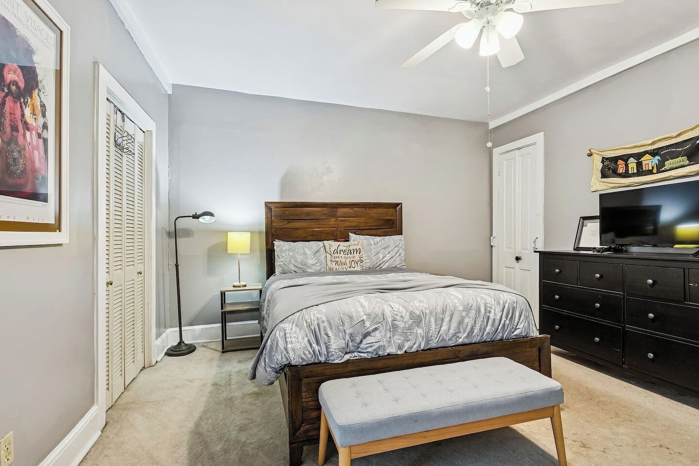 A bedroom with a bed, a nightstand, a lamp, a dresser, and a ceiling fan.