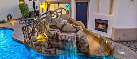 A swimming pool with a rock waterfall feature and a patio area with outdoor seating.