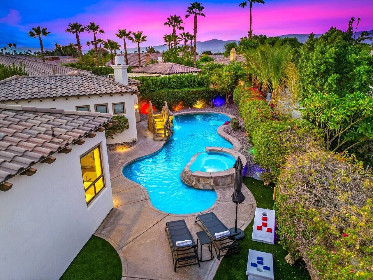 A swimming pool with a hot tub, surrounded by lush greenery and palm trees.