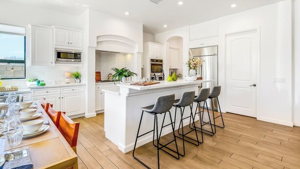 Een moderne keuken met witte kastjes, een centraal eiland met barkrukken, en een eethoek met een houten tafel en stoelen.