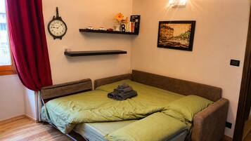 Une chambre à coucher avec un lit, une horloge, une étagère avec des livres et un vase, et un tableau encadré accroché au mur.