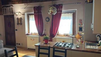Une cuisine équipée d’une cuisinière à gaz, d’une table à manger avec des chaises et d’une fenêtre avec des rideaux.