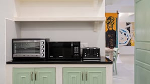 Una kitchenette equipada con microondas, tostadora y un refrigerador pequeño. Se observa un mueble verde con dos puertas y una pared blanca con un cuadro.