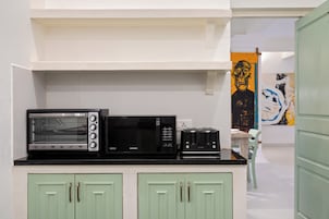 Una kitchenette equipada con microondas, tostadora y un refrigerador pequeño. Se observa un mueble verde con dos puertas y una pared blanca con un cuadro.