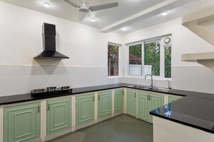 Una cocina con gabinetes verdes, encimera negra, estufa, ventana y ventilador de techo.