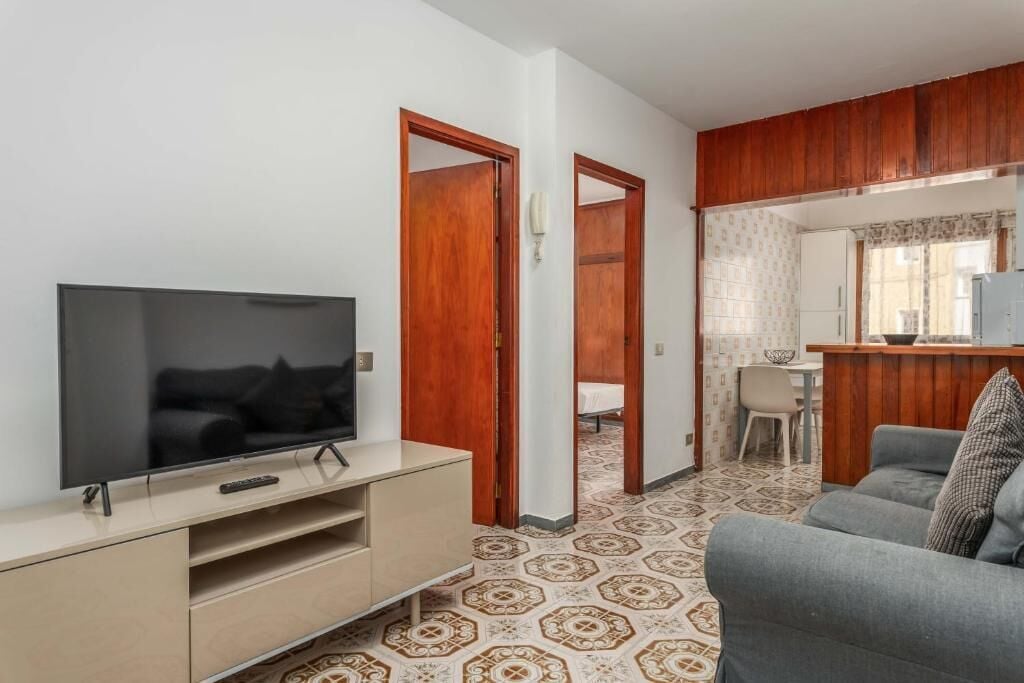 Ein Wohnzimmer mit Fernseher, Sofa und Küchenzeile mit Esstisch.