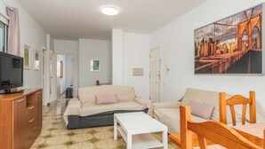 A living room with a sofa, a coffee table, and a TV on a wooden cabinet. - Edificio Los Playeros (Arona)