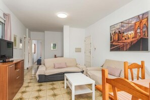 A living room with a sofa, a coffee table, and a TV on a wooden cabinet. - Edificio Los Playeros (Arona)