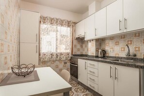 A compact kitchen with white cabinets, a granite countertop, and patterned tile flooring. - Edificio Los Playeros (Arona)