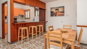 A compact kitchen with a wooden bar and stools, a dining table with chairs, and a patterned floor. - Edificio Los Playeros (Arona)