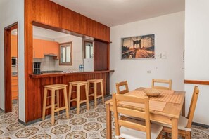 A compact kitchen with a wooden bar and stools, a dining table with chairs, and a patterned floor. - Edificio Los Playeros (Arona)