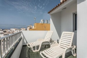 A balcony with two white lounge chairs, a tiled floor, and a view of the cityscape. - Edificio Los Playeros (Arona)
