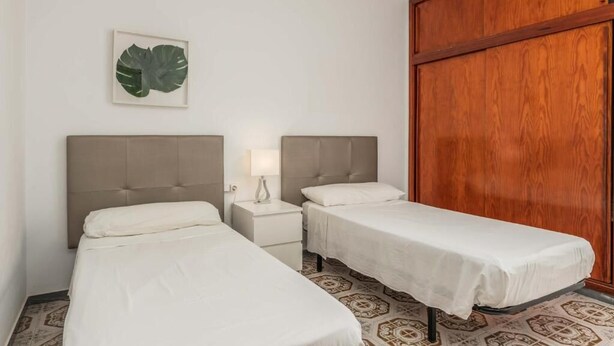 A hotel room with two single beds, a nightstand with a lamp, a wooden wardrobe, and a large decorative leaf on the wall. - Edificio Los Playeros (Arona)