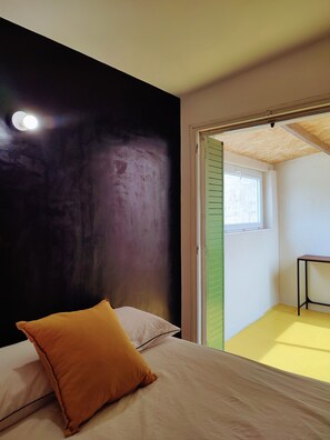 Ein Schlafzimmer mit einem Bett, einem Kissen, einem Fenster und einer Tür zu einem weiteren Raum.