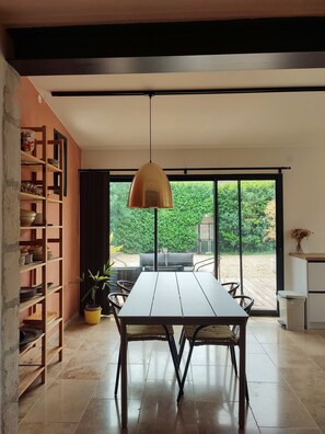 A modern dining area with a table and chairs, a hanging pendant light, and a view of a garden through large glass doors. - A charming house in earthy tones with an intimate garden where you can relax (Avignon)
