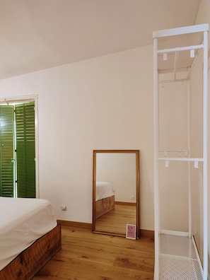 Ein Schlafzimmer mit einem hölzernen Bett, einer grünen Tür, einem weißen Kleiderschrank und einem Spiegel.