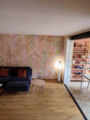 A living room with a sofa, a round table, and a wall with shelves containing plates and glasses. - A charming house in earthy tones with an intimate garden where you can relax (Avignon)
