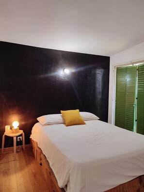 A bedroom with a bed, a nightstand with a lamp, and a green door. - A charming house in earthy tones with an intimate garden where you can relax (Avignon)