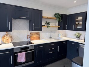 A modern kitchen with black cabinets, a white countertop, a built-in oven, and a stainless steel sink. - Beautiful Cotswold Cottage | Sleeps 6-8 | Near to Elkstone Studios (Winstone)