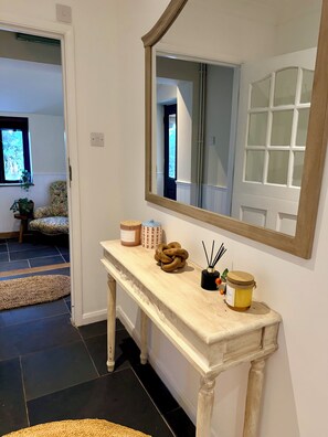 A hallway with a white console table, a mirror, and a door leading to another room. - Beautiful Cotswold Cottage | Sleeps 6-8 | Near to Elkstone Studios (Winstone)