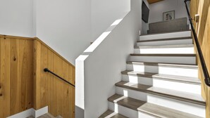 Eine Treppe mit Holzhufen und einer Handlauf, die zu einem Raum führt, in dem ein Deckenventilator und ein gerahmtes Bild zu sehen sind.