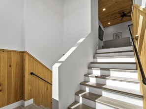 Eine Treppe mit Holzhufen und einer Handlauf, die zu einem Raum führt, in dem ein Deckenventilator und ein gerahmtes Bild zu sehen sind.