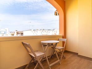 Un balcón con dos sillas de madera y una pequeña mesa redonda, con vistas a un paisaje urbano.