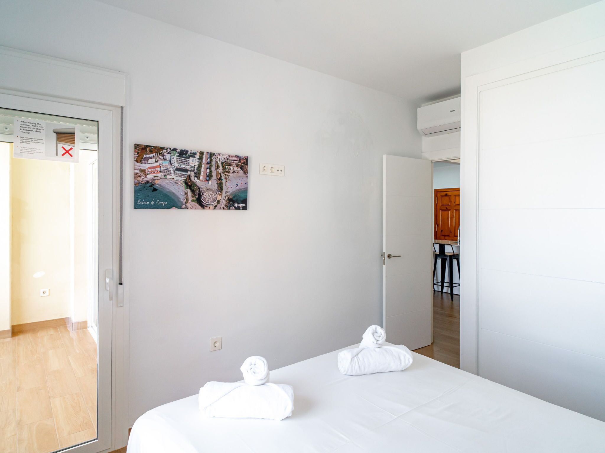 Habitación de hotel con una cama, dos toallas, un cuadro y una puerta que da a una zona de cocina.
