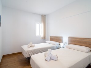 Ein Hotelzimmer mit zwei Betten, einem fensterbelaubten Fenster, einem Nachttisch mit Lampe und Holzboden.