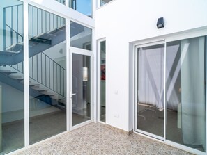 Ein modernes Gebäude mit Glastür, die zu einem überdachten Außenbereich, einer Treppe und einer wandmontierten Leuchte führt.