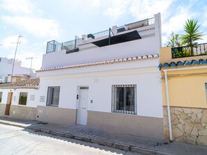 Um edifício de dois andares com telhado plano, uma varanda no andar superior e uma pequena porta de entrada.
