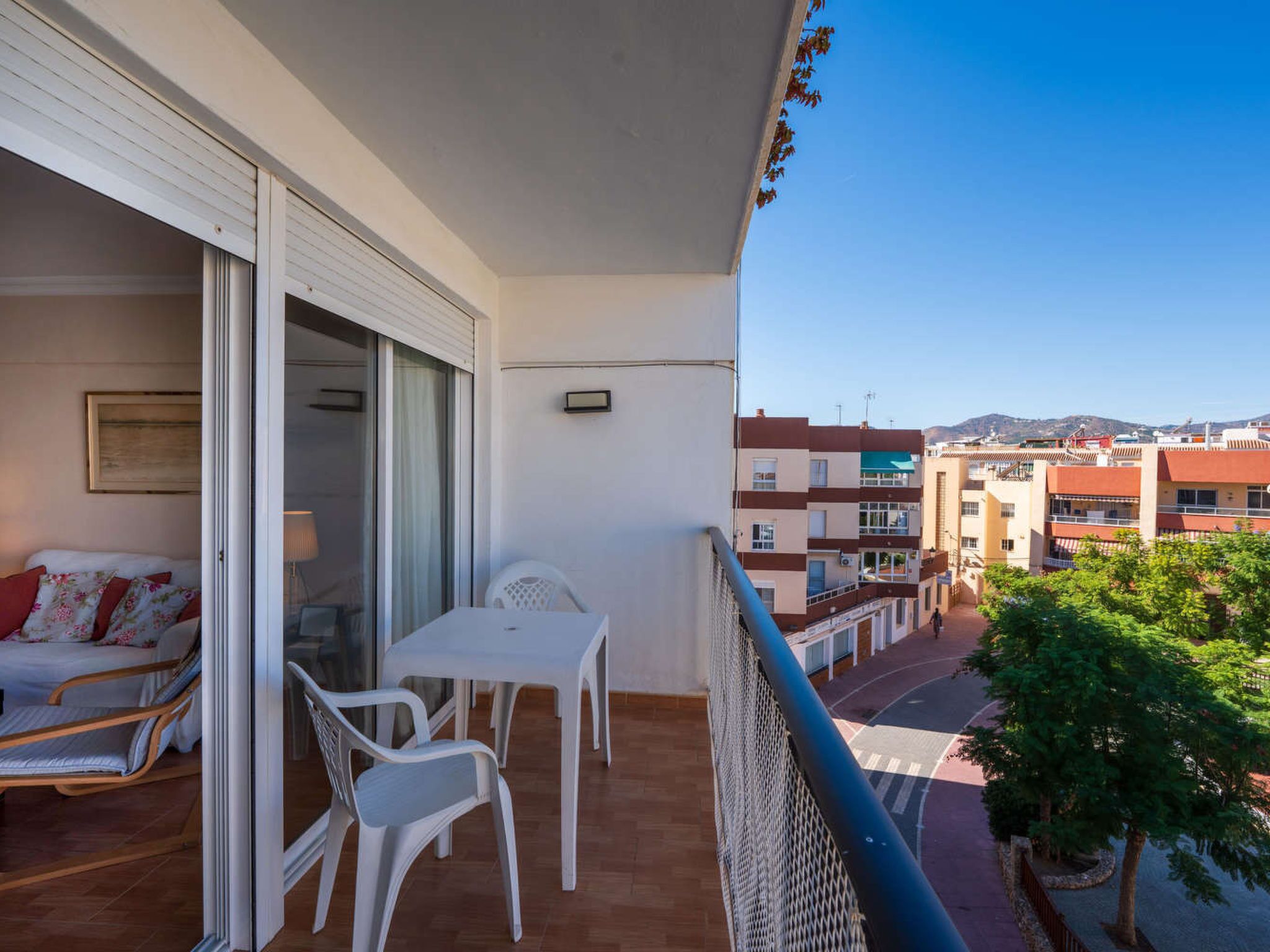 En balkon med et bord, stole, en sofa og udsigt til gaden og bygningerne.