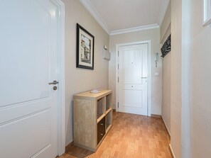 Ein schmales Dielenbett mit Holzboden, weißen Türen, einer kleinen Holzablage mit einer Schale und einem gerahmten Bild an der Wand.